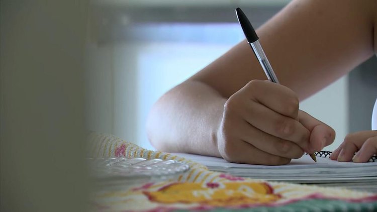 Adolescente escreve em caderno