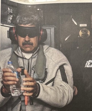 Nicolás Maduro, algemado e vendado, envolto em um casaco cinza Nike Tech Fleece